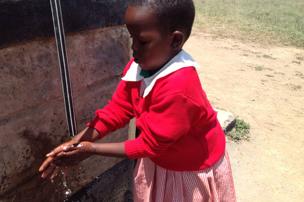 Young girl washing her hands at a water well.