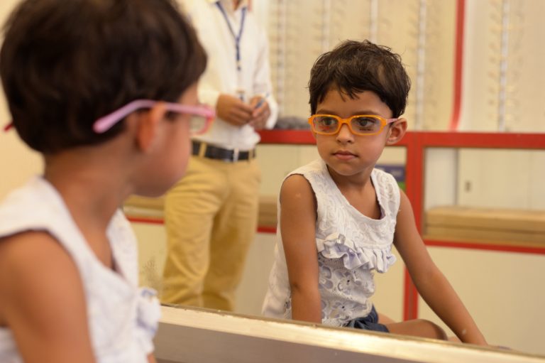 Child, wearing eyeglasses, looking at her reflection in a mirror