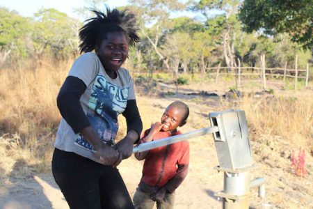Children smile at the camera as they collect water from a borehole