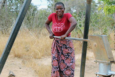 A woman collects water from a borehole and smiles at the camera