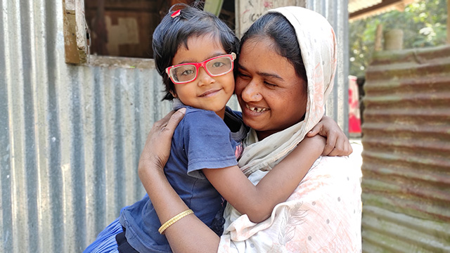 A mother smiles as she holds her daughter who is wearing a new pair of eyeglasses