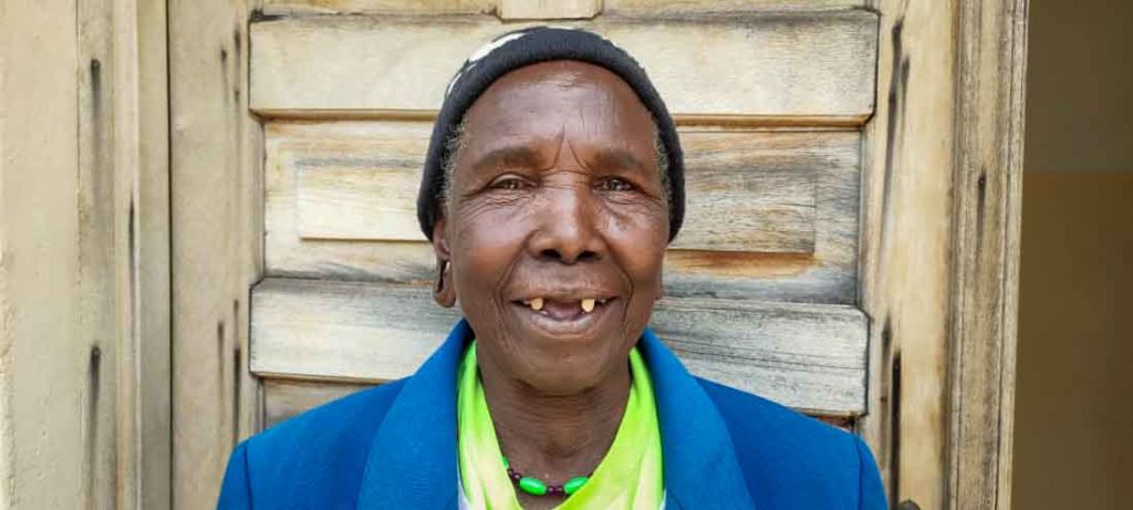 An elderly woman wearing a blue jacket smiles at the camera.