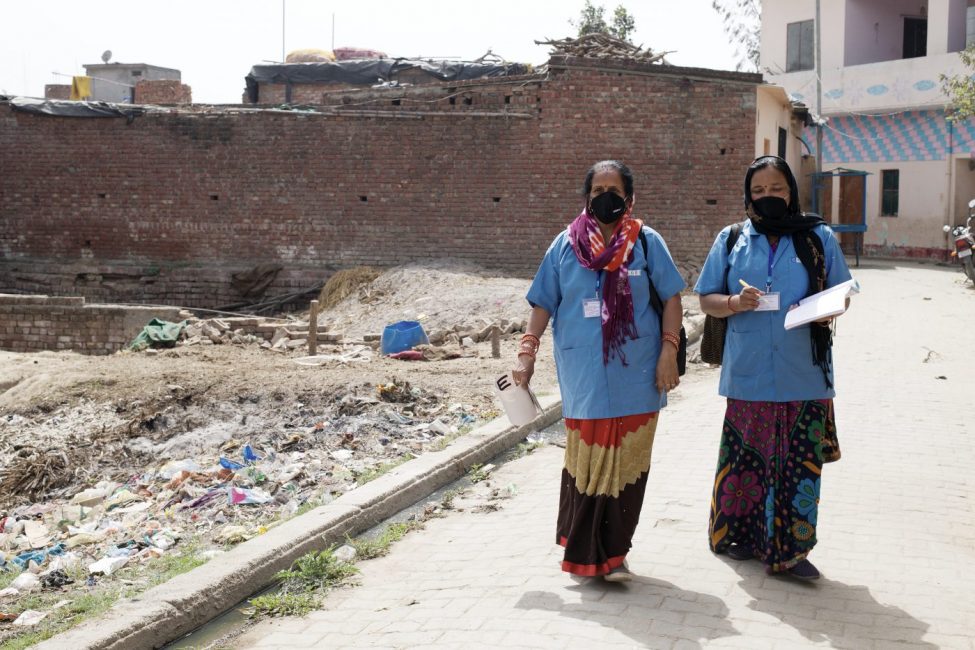 Two community health workers walks through a village in India during a door-to-door survey