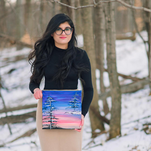 Portrait of Neya Chander as she smiles at the camera holding a painting on canvas