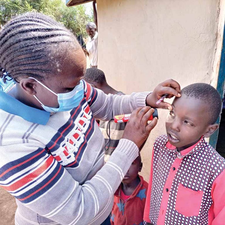 A community health worker checks the right eye of a young boy using a flashlight