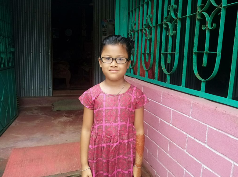 A child, wearing eyeglasses, looks at the camera