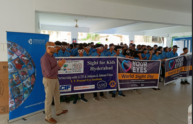 A group of more than a hundred students dressed in blue uniforms and wearing heart-shaped glasses proudly display World Sight Day banners.