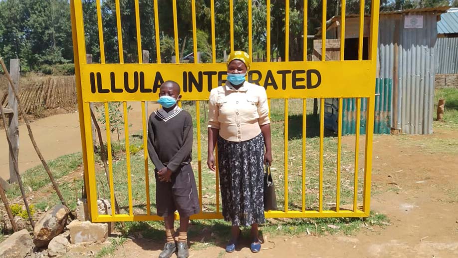 Paul and his mother stand togteher in front of a yellow gate, posing for a photo. 