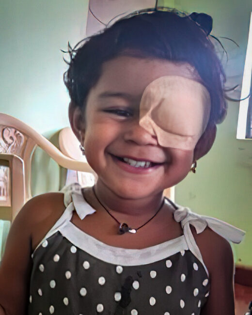 A smiling toddler is held by her mother. The little girl has a patch over her right eye.