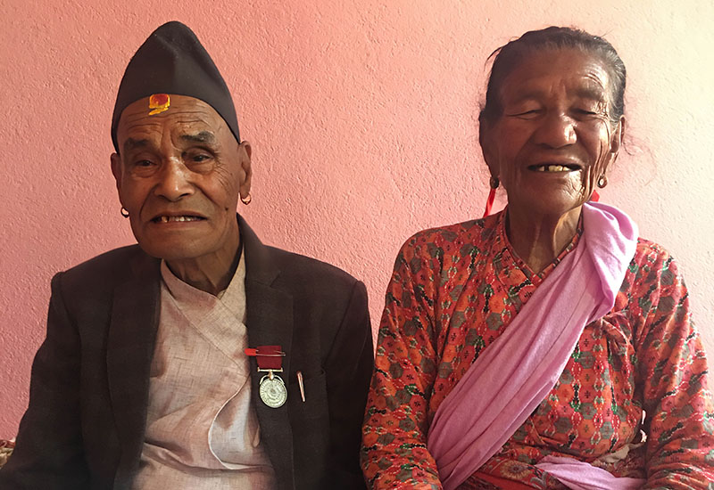 An elderly man and woman sit together posing for a photo.
