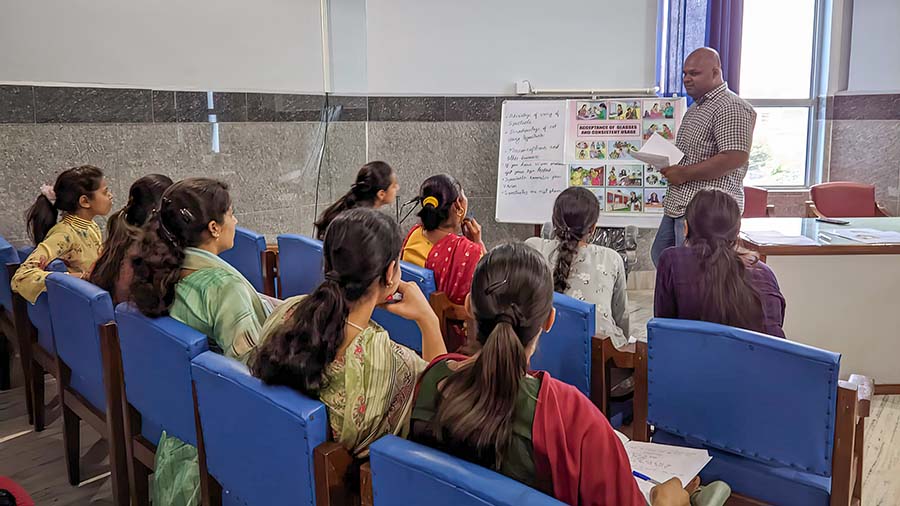 An Operation Eyesight employee stands at the front of the room showing a poster to a group of community health workers who sit in blue chairs, listening and taking notes.