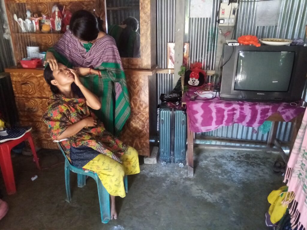 A woman wearing a green sari, from Bangladesh, applies eye makeup to another woman, at a home beauty studio. 