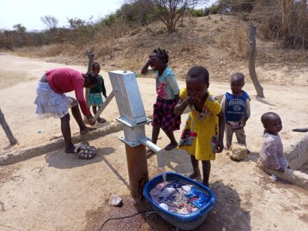 Children joyfully splash water on the faces at the newly-rehabilitated borehole in the village of Lukanda B, Zambia.