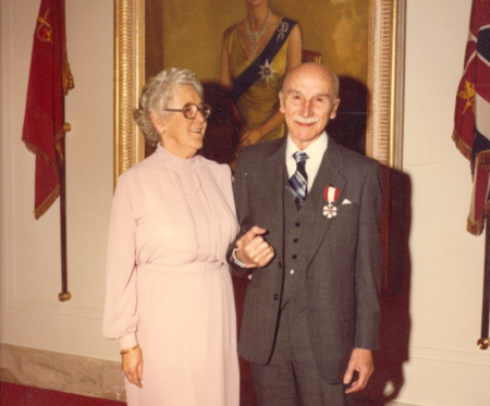 Dr. Ben Gullison and his wife Evelyn stand together in front of a portrait of Queen Elizabeth.