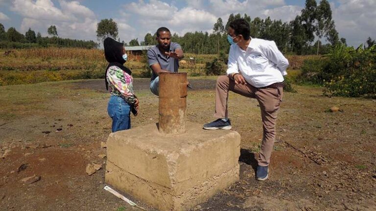 A woman and two men stand near a borehole in rural Ethiopia, engaged in a discussion. 