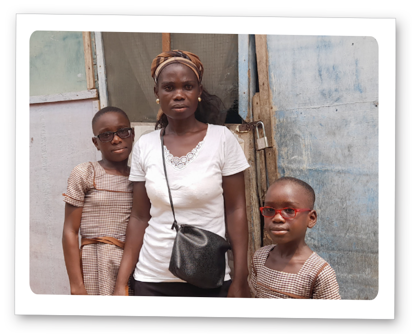 Two girls, wearing eyeglasses, stands with their mother in front of their home