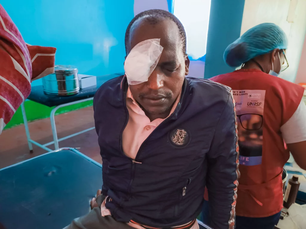 A man sits on a gurney in a clinic. He has a bandage over his right eye.