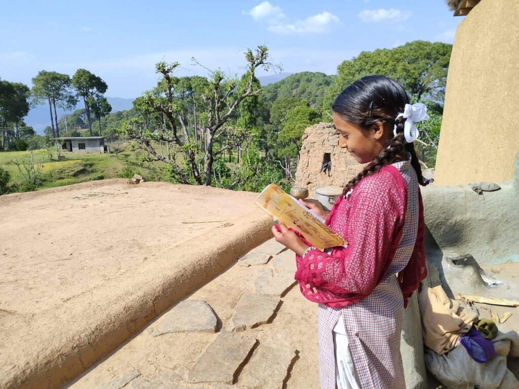 A young girl stands at a balcony reading a book, smiling.