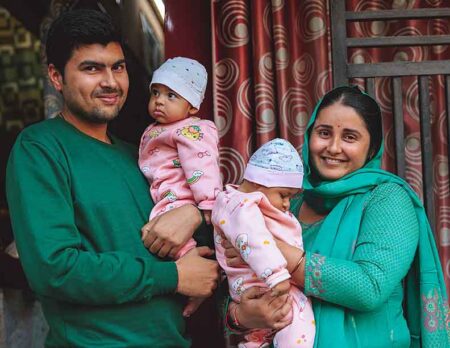 Family smiling while carrying twin girls in Moradabad, India.