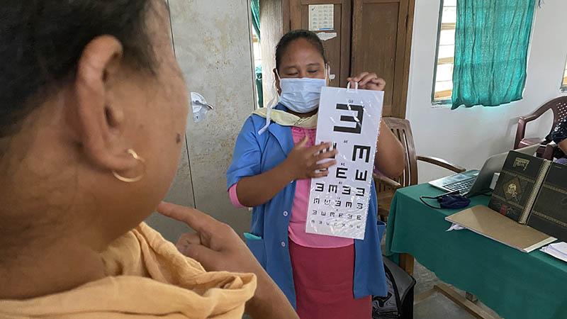 A female health worker holds up an eye chart for a female patient.
