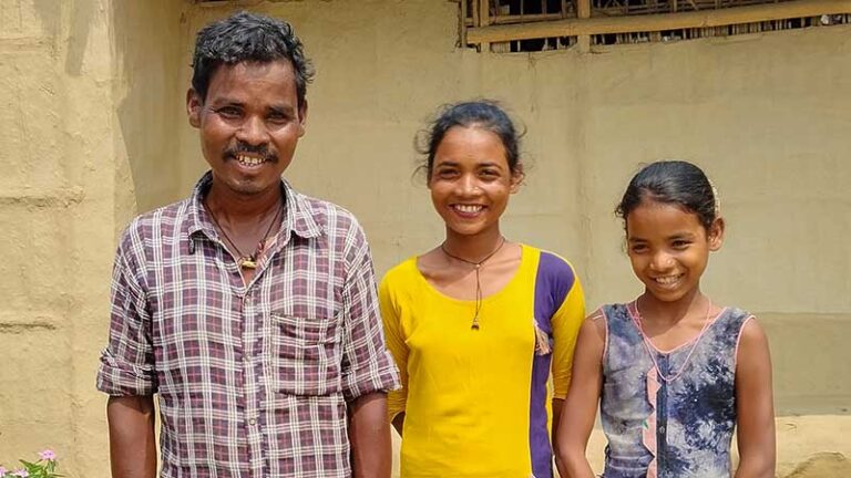 Man stands with his two daughters beside him, smiling.