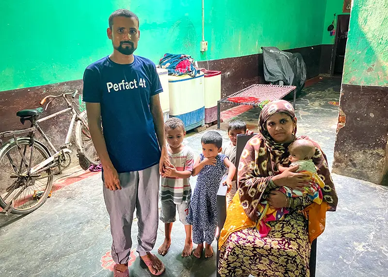 A family of three children, an infant and their mother and father pose for a photo inside their home.