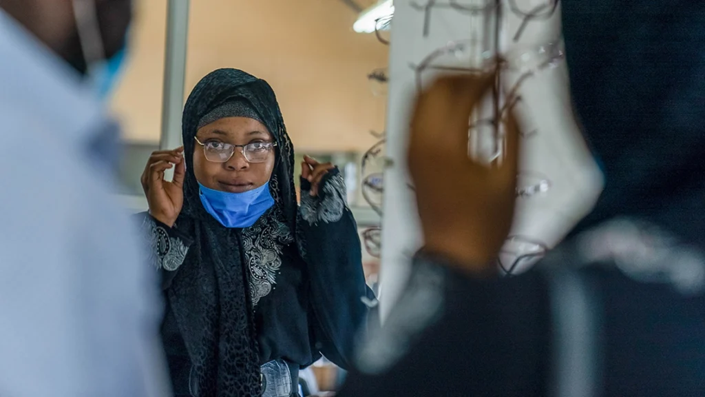 A woman tries on a pair of eyeglasses in front of a mirror.