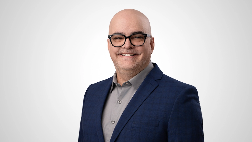 A man wearing eyeglasses poses for a head shot. He is smiling.