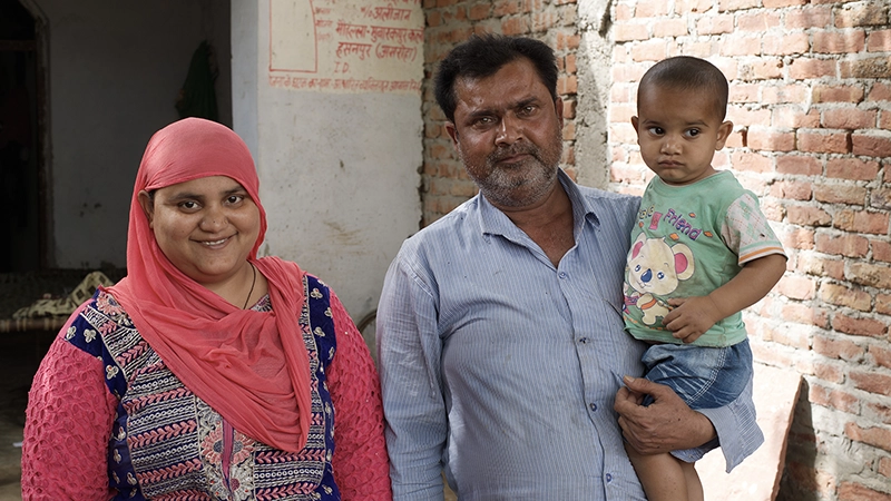 A man poses for a photo with his wife. He holds a toddler in his arms.
