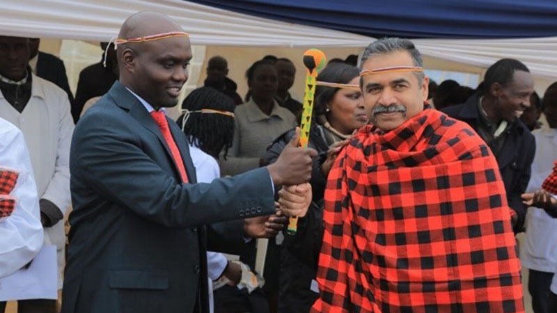 Two men hold a beaded staff together.