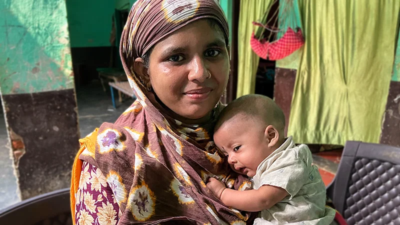 A woman hugs a small baby close her to chest.|A woman cradles an infant while sitting in a chair. A toddler stands next to them.|A group of professionals sits around a board room table.|Three panel collage shows a medical device at far left