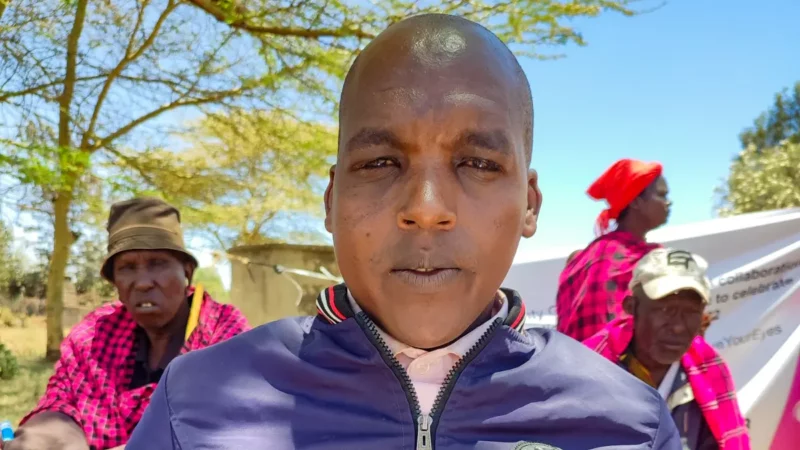A young man wearing a blue jacket looks into the camera. There are people