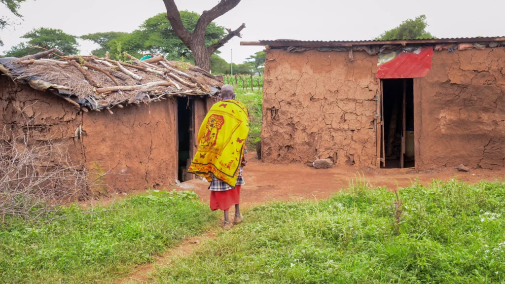 A woman walks towards a house in a village.||A Masaii family poses for a photo.|A woman smiles at the camera. She has a cloudy left eye.|