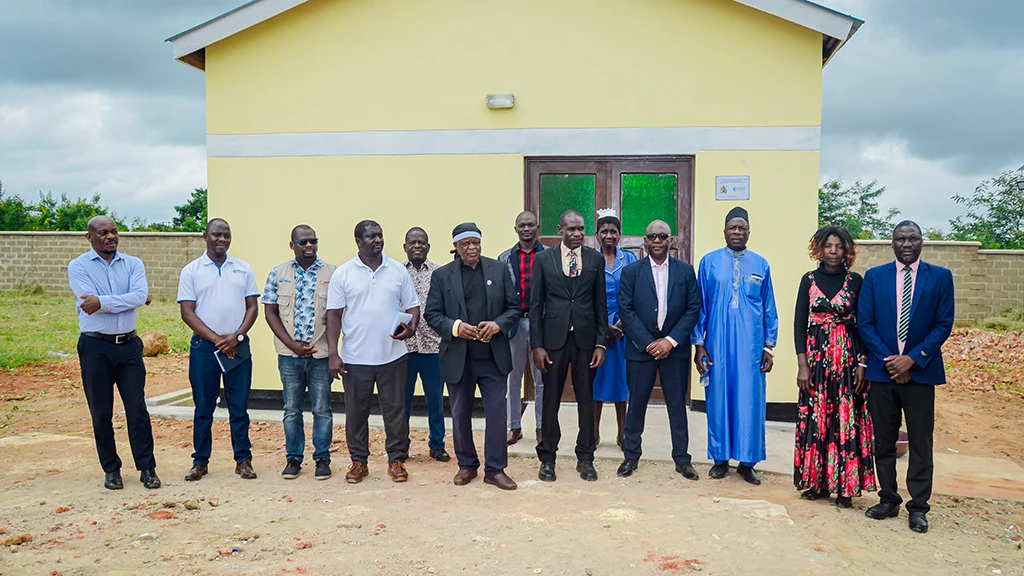 A group of men and women stand in front of a small clinic painted yellow.||A group of men and women stand before a newly-painted yellow building.