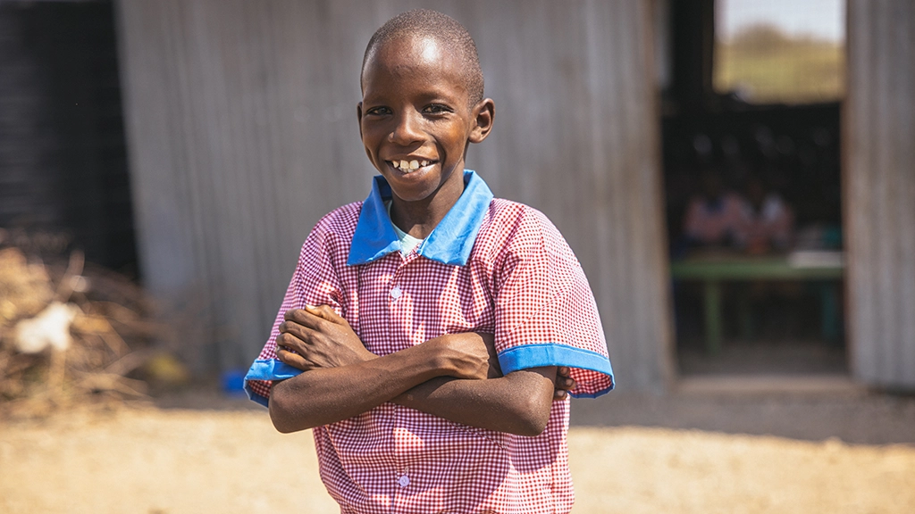 A boy in a blue and red school uniform shirt stands with his arms crossed