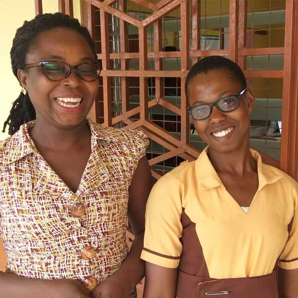 A young girl poses for a photo with her teacher. Both of them are wearing eyeglasses.|Jennifer stands with her teacher