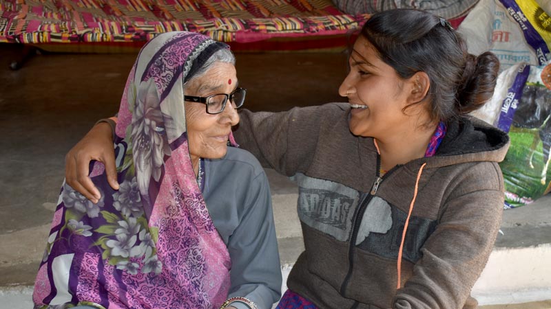 A young woman hugs and smiles at a senior woman wearing eyeglasses|A senior woman