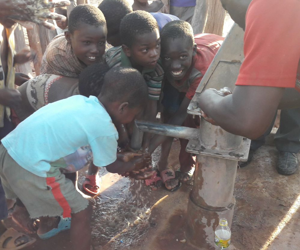 Muuka village children eagerly reach for clean water now flowing from a fixed water pump.|Women of Muuka village in Zambia watch as the water pump in their village is fixed.