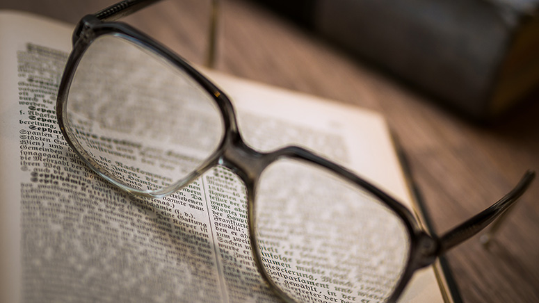 A pair of eyeglasses sit on an open book|A teenaged girl stands posed for a photo in a wooded area